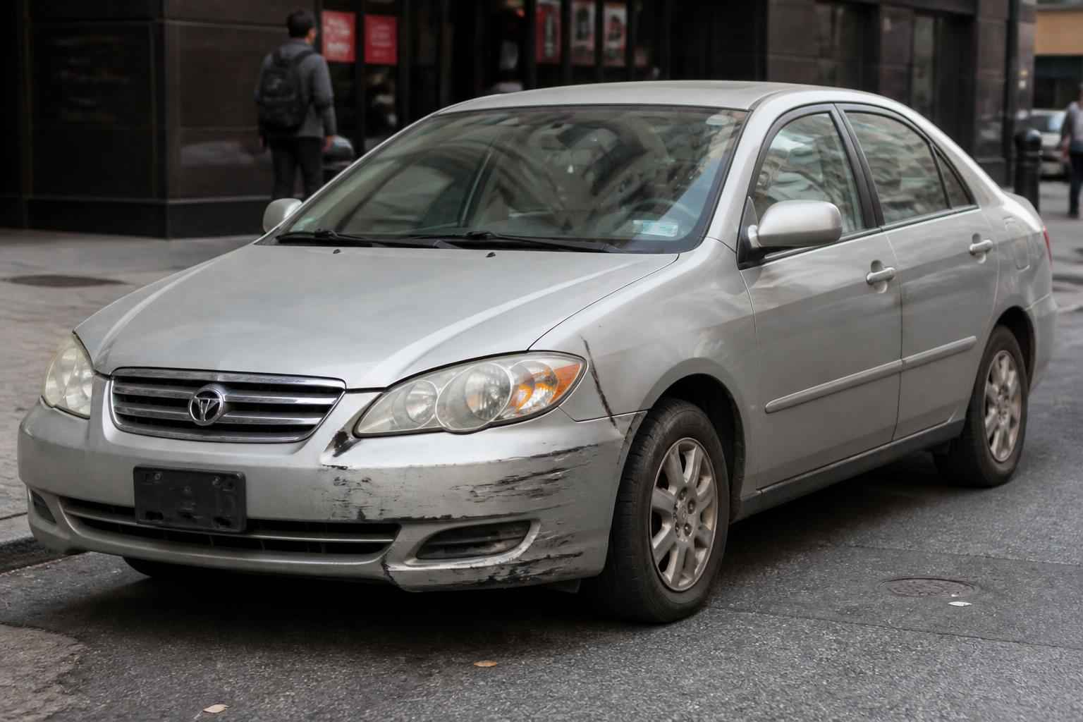 Srebrna Toyota Corolla sedan z porysowanym i wgniecionym przednim zderzakiem na miejskiej ulicy